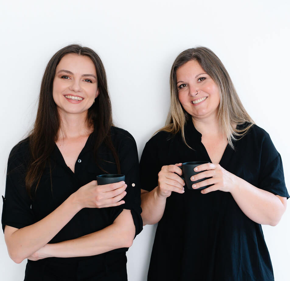 Die Agilistas Anna und Beatrix halten eine Tasse Kaffee in der Hand und lächeln fröhlich